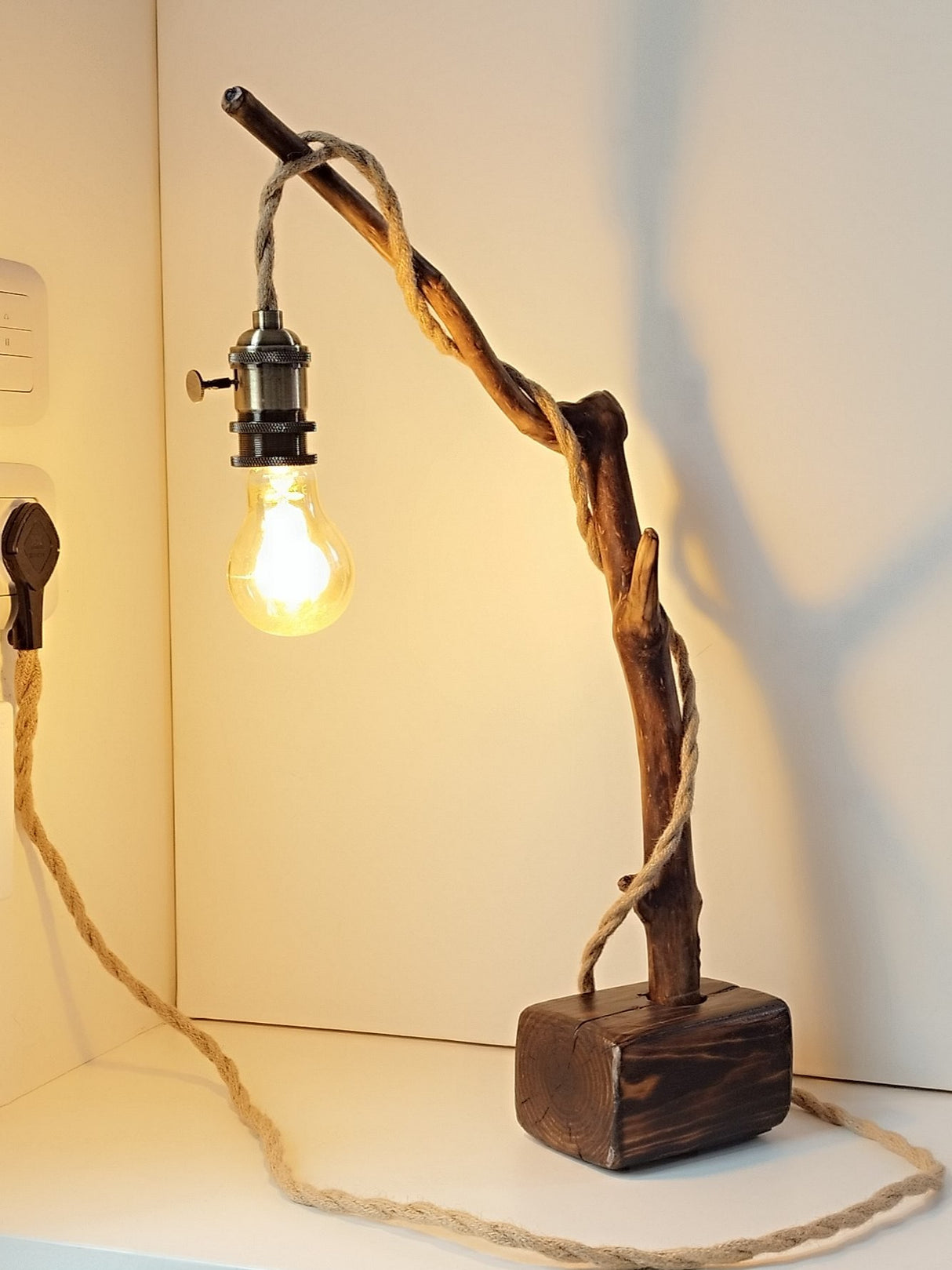 Lámpara de mesa artesanal Raiz de Luz hecha de madera flotante carbonizada Yakisugi y cable de cuerda de yute sobre fondo blanco.