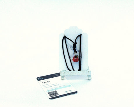 Collar artesanal rojo modelo Sua de la Serie Singularidades por Isabel Nobre, modelado en pasta de papel con cordón negro y certificado de autenticidad sobre expositor blanco.